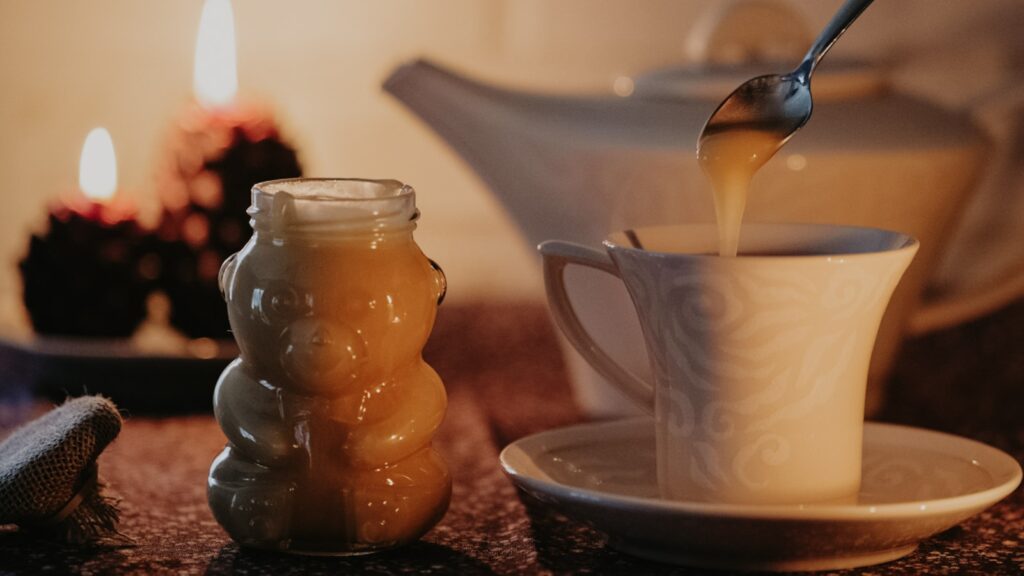 Honey is spooned into tea from a fun bear-shaped honey jar.